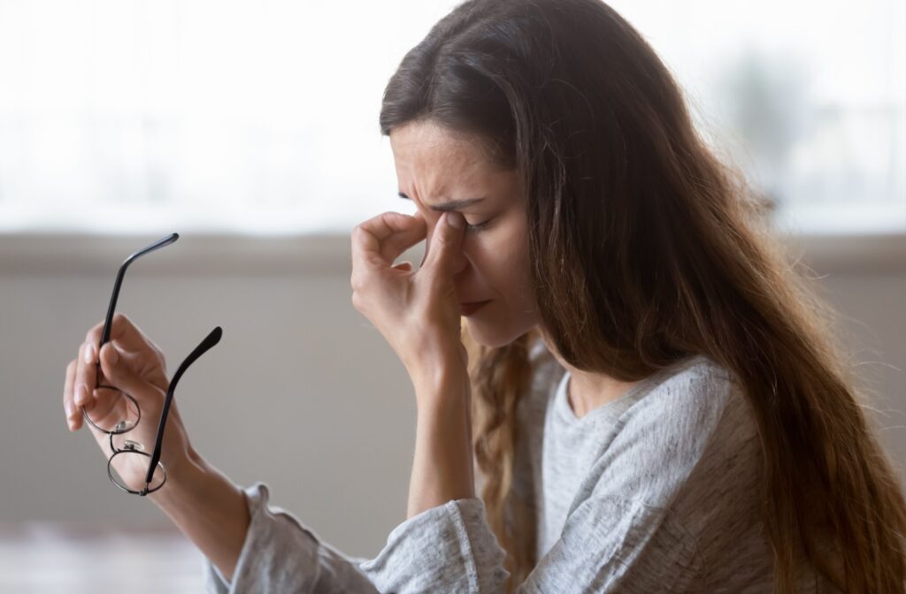 Woman rubbing her eyes with her glasses off, experiencing blurry vision caused by dry eye.