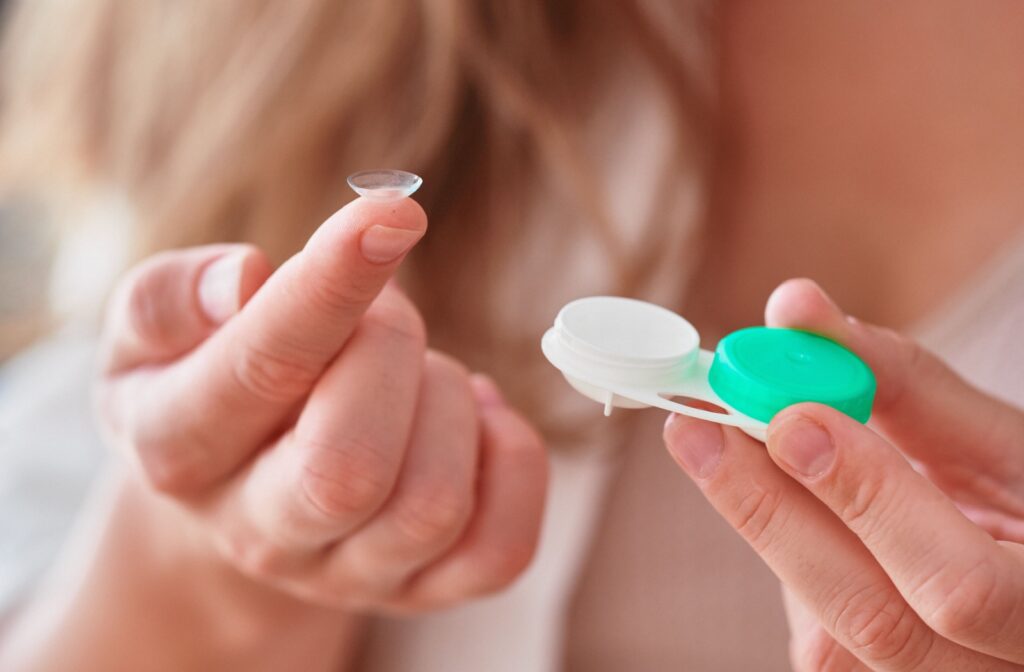 Person holding a soft contact lens on fingertip next to an open contact lens case with green and white caps.